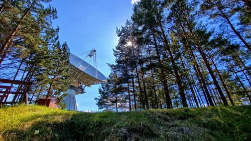 Télescope RT-32 capturant une vue à faible angle entouré de grands arbres à Irbene, en Lettonie, pendant la journée