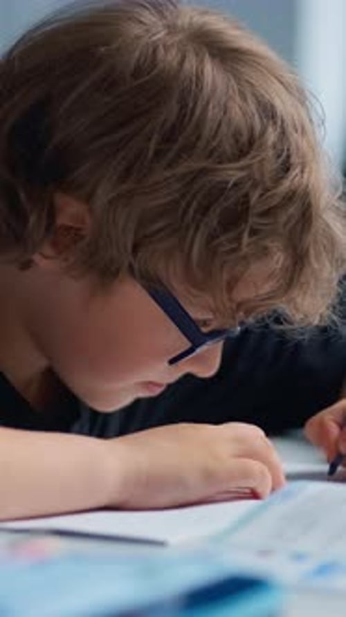Closeup Images of a Young Boy Wearing Glasses Focused Intently on Writing or Drawing on Paper at a