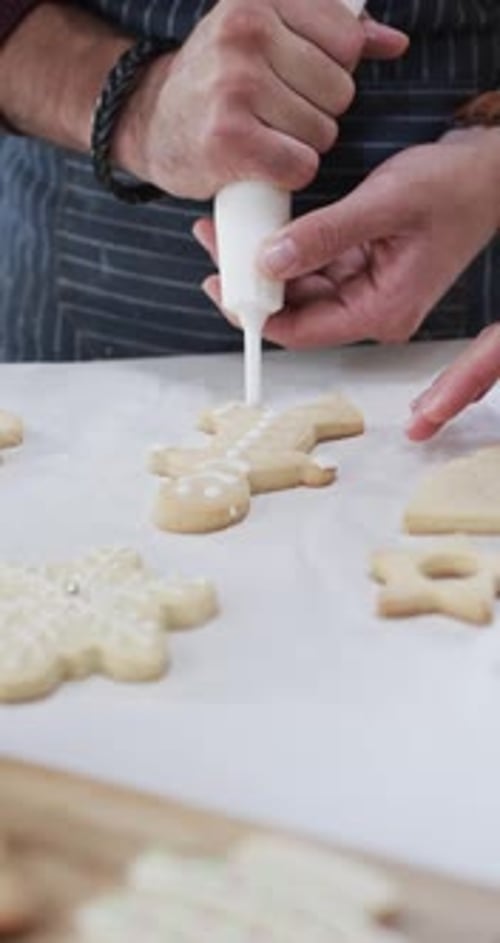 Vertical video of midsection of caucasian man decorating christmas cookies, slow motion