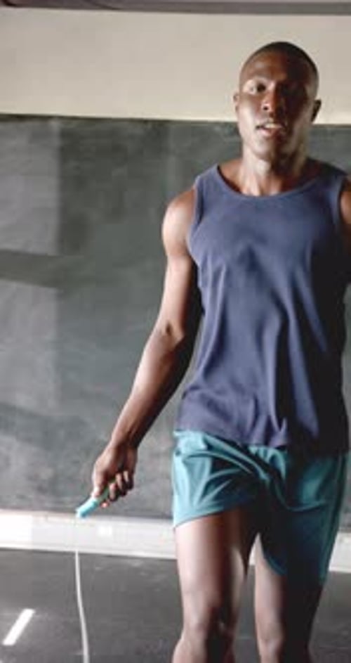Vertical video: Athletic man jumping rope in gym, focused on fitness and endurance training