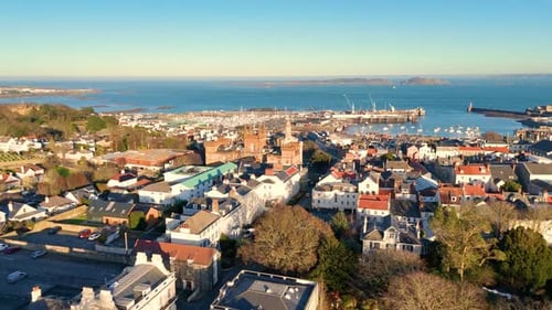 High backwards drone footage of the roof tops of St Peter Port Guernsey in the golden hour with exte