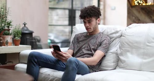 Young Man Relaxing on Sofa Using Smartphone