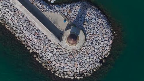 Aerial Video of a White Lighthouse With a Flag Standing in a Bay Surrounded By Calm Blue Waters