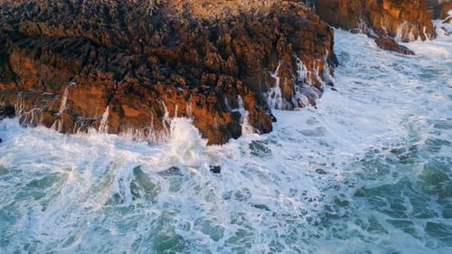 Rough marine waves foaming on stony shoreline crashing at seashore rocks drone view