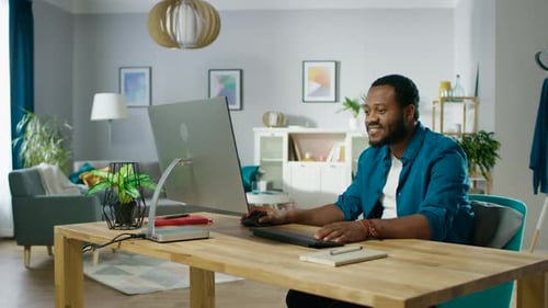 Handsome Black Man Works on a Personal Computer while Sitting at the Desk of His Cozy Living Room.