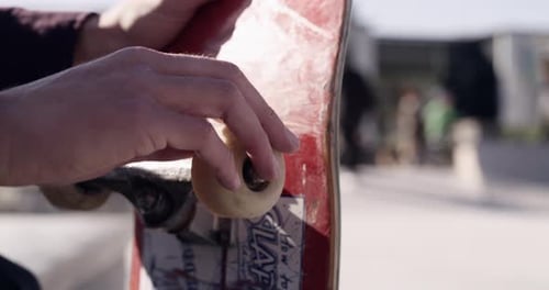 Hands Adjusting Skateboard Wheels on Sunny Day