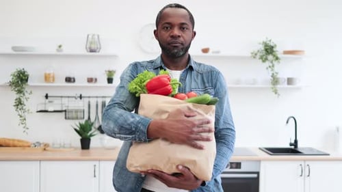 Man Smiling Holding Groceries in Modern Bright Kitchen