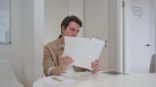 Frustrated Man Reading Documents at Office Desk