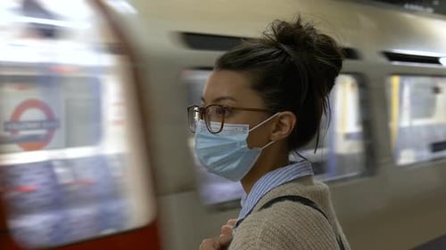 Woman in face mask waiting for tube train in underground station. Coronavirus metro travel. Covid-19