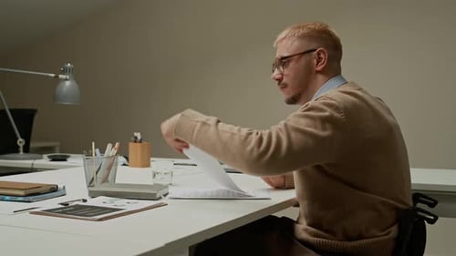 Male Manager in Wheelchair Passing Paper to Colleague Working at Desk in Office