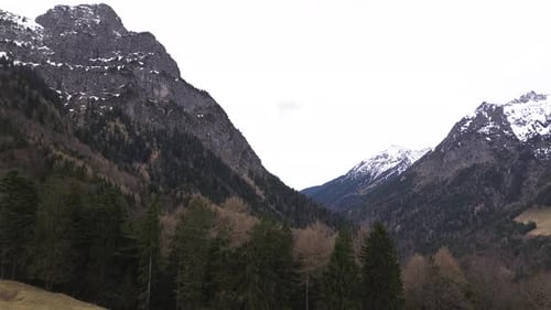 Drone rise up to summit cross towards snow covered mountains surrounded with pine forest in Austria