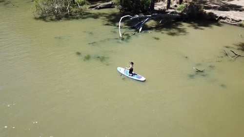 Vista aérea de un Zumbido sobre el río con una mujer usando una tabla de surf