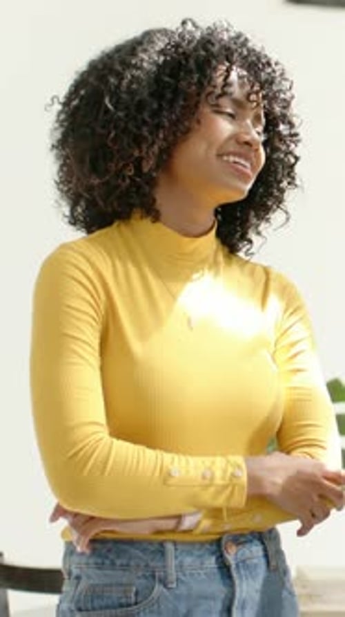Vidéo verticale : Une femme en haut jaune se déplace et se retourne, souriant au comptoir en réponse à une voix invisible