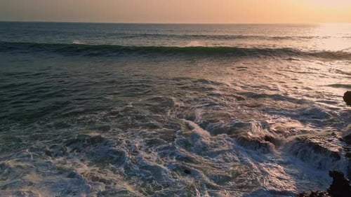 Golden summer sundown aerial view over ripple sea surface washing rocky coast