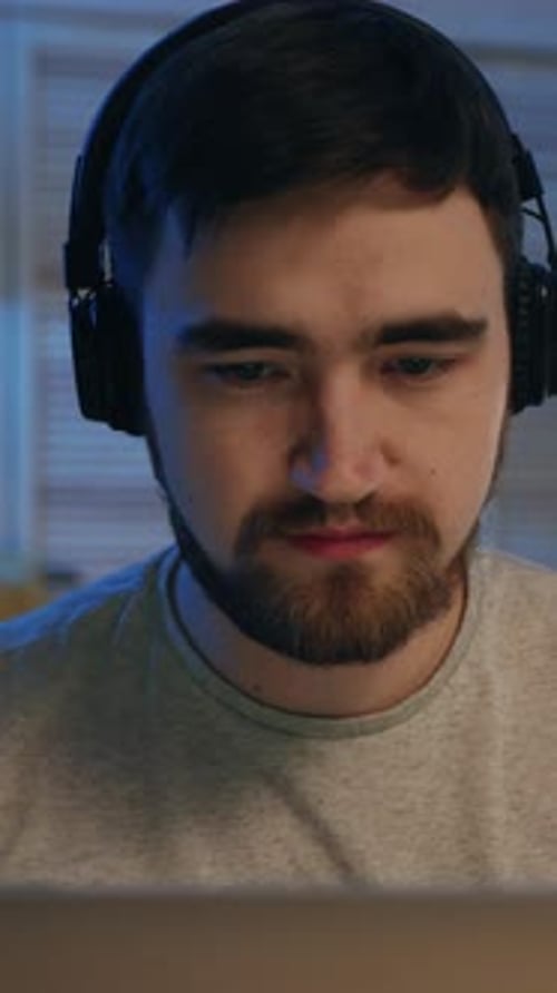 A Focused Young Man Working Diligently on His Laptop Simultaneously While Wearing Headphones