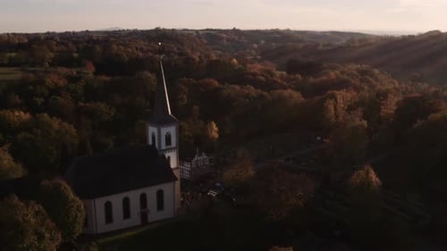 Aerial shot of white german catholic church in front of forest during sunset