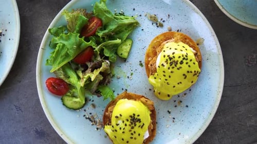A top view of a plate with gourmet eggs benedict and vegetable salad, rotating