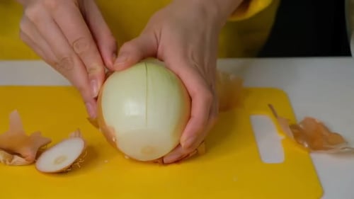 Hands Peeling a White Onion on Cutting Board