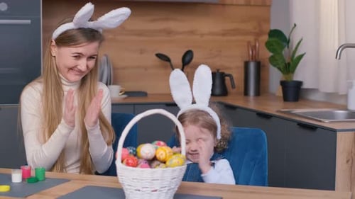 A Woman and a Girl in Bunny Ears at a Table with Easter Eggs