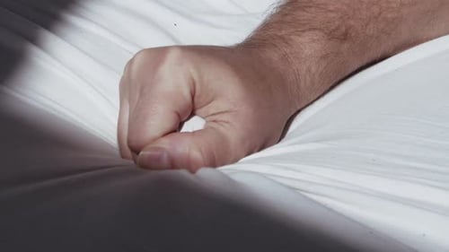 Close up of male hand grasping the bedsheet while reaching climax during sex
