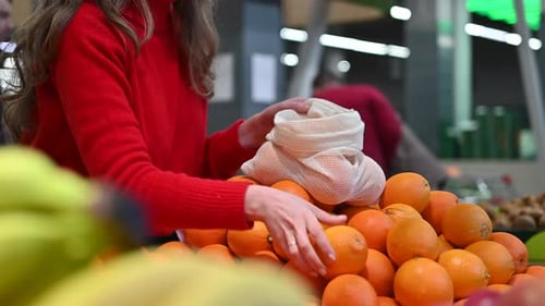 Mujer recogiendo naranjas en una bolsa reutilizable en una tienda. Temáticas del Día de la Tierra y la Ecología. Cámara lenta
