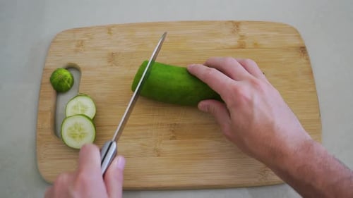 First Person POV View of Man Slicing Cucumber on Wooden Cutting Board with Knife