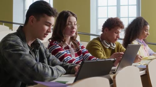 Gen Z Peers Sitting at Tiered Desk Studying in Lecture Hall with Gadgets