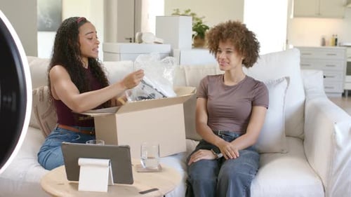 Des femmes afro-américaines déballant un nouveau colis sur un canapé, déchirant un film à bulles, révélateur, appareil pour vlog