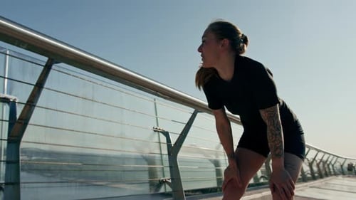 Fitness young sportswoman girl tired after doing sports training outdoors in the city on the bridge