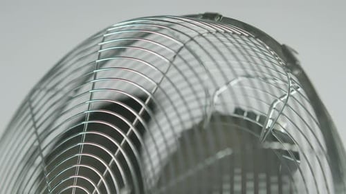 Zeitlupe verlangsamt schwarze Lüfterblätter eines metallischen Ventilators vor weißem Hintergrund