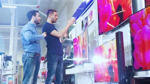 In the Electronics Store Professional Consultant Shows Latest 4K UHD TV's to a Young Man, They Talk