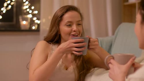Freundschafts-, Hygge- und Pyjama-Party-Konzept — Glückliche junge Frau oder junges Mädchen trinkt Tee und...