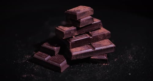 Chocolate Pieces Rotating Background with Cocoa Powder. Chunks of Sweet Dark Chocolate Turning