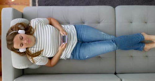 Woman Reclines on Couch with Headphones and Phone