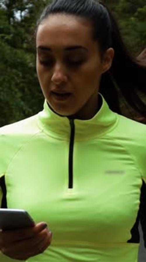 Vertical de Happy Fit Woman Runner Olhe para seu celular enquanto corre