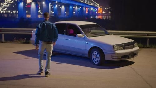 Man Walking to Car, Woman Inside, at Night