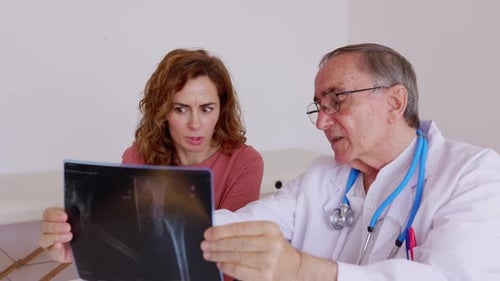 Senior Doctor with Female Patient Looking at Xray at Medical Consultation