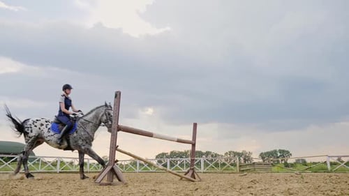 Eine Jockeyfrau springt in einem Springwettbewerb in Zeitlupe über die Barrieren auf einem Pferd