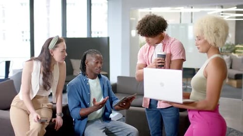 Discussing project, diverse team collaborating in office using tablet, smartphone, and laptop