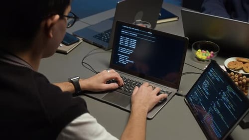 Web Engineer Working on Laptop with Code Running on Screen in Dimly Lit Office
