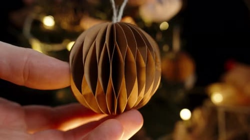 Hand Turns Paper Christmas Ornament on Tree