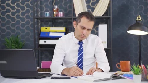 Man Works at Desk Writing in Notebook