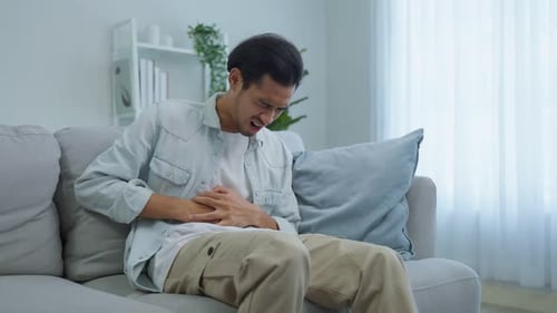 Asiatische attraktive kranke Männer leiden im Wohnzimmer unter Magenschmerzen.