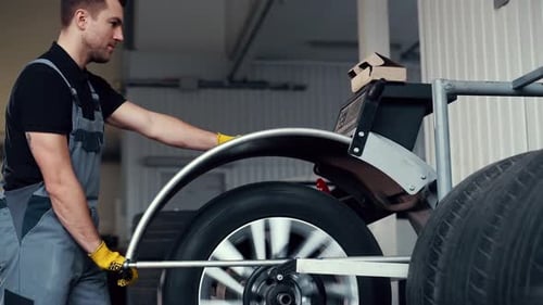 Putting wheel into automatic rolling device. Man in uniform is in the automobile repair shop