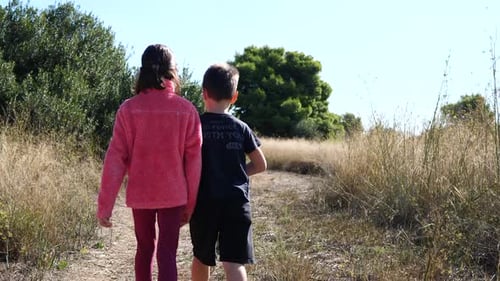 Young kids brother and sister walking together on a path. Slow-motion gimbal shot.