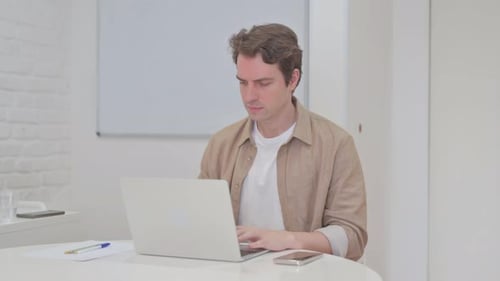 Young Man Leaving Workspace after Closing Laptop