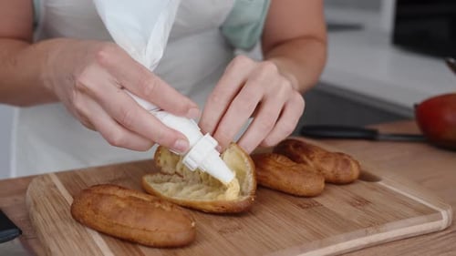 Woman Decorating Eclairs with Cream in Kitchen