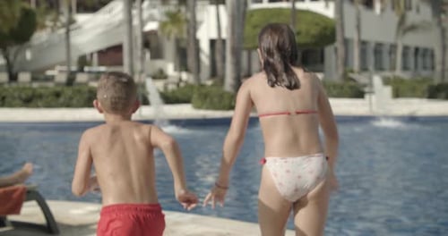 Close Up Young Kids Jumping Into Resort Pool Brother and Sister Above