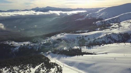 Aerial view of snowy mountains overlooking valleys and clouds at sunset
