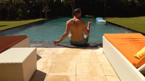 Man Relaxing by the Pool Using Mobile Phone